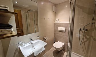 A modern bathroom with a shower cubicle, sink, and toilet. Bright tiles and a large mirror create a pleasant atmosphere.