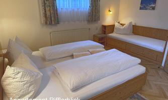 A cozy bedroom with two single beds and an additional bed. Bright walls and a window provide friendly light.