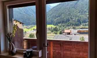 A view of the mountains through an open window. In the foreground, stylish home accessories and a balcony are visible.