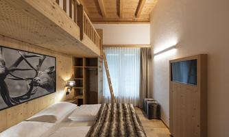 A modern room with wooden decor and a cozy loft area. It features a large window that lets in plenty of light, as well as a TV and a wardrobe.
