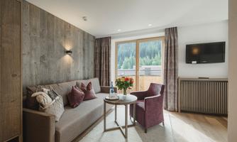 A modern living room with a cozy sofa and two armchairs. Large windows provide a view of the surrounding nature.
