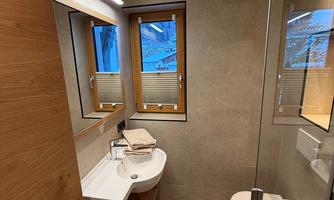 A modern bathroom with wooden details and large windows. There is a sink, a toilet, and a shower.