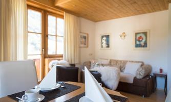 A cozy living room with a dining table and seating area. The room is bright and friendly with large windows and tasteful decoration.