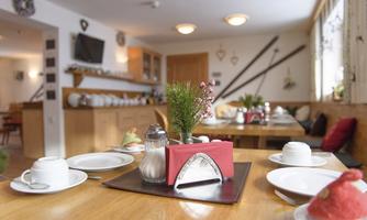 A cozy breakfast room with wooden tables and a fresh table decoration. The tables have dishes and a small plant as a centerpiece.