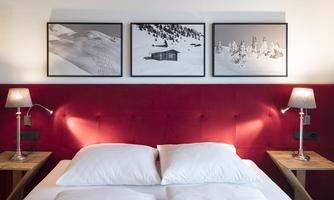 A cozy bedroom with a red headboard and two nightstands. On the wall hang three black-and-white pictures of snowy landscapes.