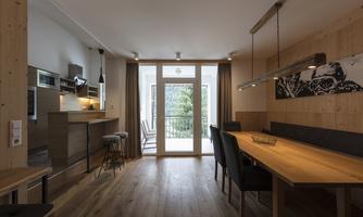 A cozy kitchen with a large dining table and modern furniture. There is a lot of wood and a large window door that lets in light.
