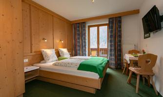 A cozy room with two beds and wooden furniture. There is a small table and a balcony door that lets in natural light.