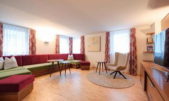 A stylish living space with colorful seating furniture and a round rug. Large windows provide plenty of natural light.