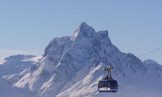 A cable car glides over snow-covered mountains under a clear sky. The majestic peaks rise high and offer an impressive view.