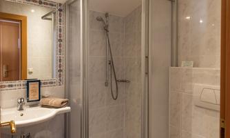 A modern bathroom with a glass shower cabin and bright tile design. A towel is placed on the sink, and there is a mirror on the wall.