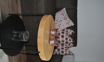 A living area with a gray couch and decorative cushions. A round table made of wood and metal stands in the center, decorated with candles.
