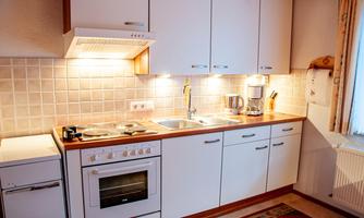 A modern kitchen with white furniture and wooden surfaces. It is well-lit and equipped with cooking appliances.