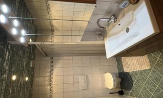 A modern bathroom with white tiles and an elegant wooden shelf. It is brightly lit and features a shower and a sink.