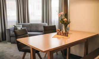 A cozy living space with a wooden table and chairs. On the table, there is a vase with flowers and the word "Relax".