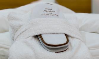 A cozy bathrobe and slippers are lying on a bed. In the background, a warm and relaxing atmosphere can be felt.