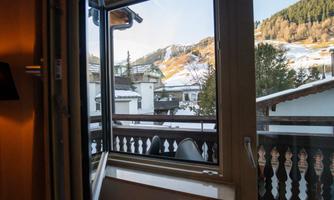 A window view of a snowy mountain landscape. In the foreground, balconies and houses can be seen.
