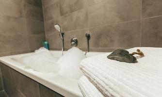 A bathroom with a bathtub full of foam. On it lie fresh towels and a nice stone.