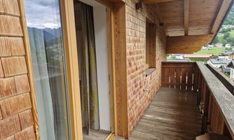 A balcony with wooden walls and a view of the mountains. The glass door leads inside.