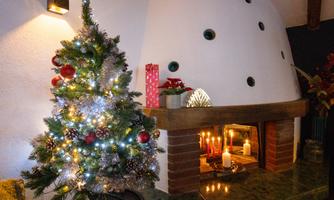 A beautifully adorned Christmas tree with lights stands next to a fireplace. The fireplace is decorated with candles and ornaments, creating a cozy atmosphere.