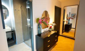 A modern bathroom with a shower and a large mirror. The entrance area is stylishly decorated with a dresser and a flower vase.