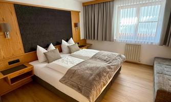 A modern hotel room with a double bed and bright wood design. Curtains hang in front of the window, and the room is furnished in a friendly and inviting manner.