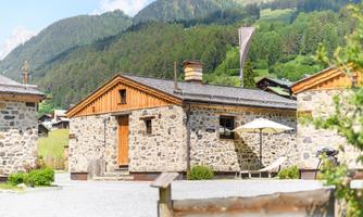 A charming stone house in a picturesque mountain landscape. There is a sunny outdoor area with a parasol and a view of the surrounding hills.