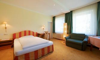 A cozy room with a large bed and a sofa. Large windows provide plenty of daylight.