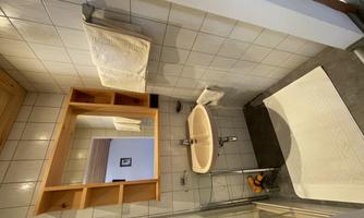 A small bathroom with a shower, a sink, and a mirror. Towels hang on the wall and a rug lies on the floor.
