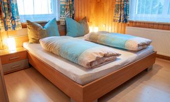 A quiet bedroom with a large double bed and bright pillows. The room has wood paneling and is well lit by windows and lamps.