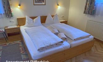 A cozy bedroom with a double bed and white bedcovers. The walls are softly decorated and the light creates an inviting atmosphere.