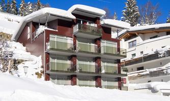 A modern building in the snow with several balconies. Surrounded by snow-covered trees and clear blue sky.