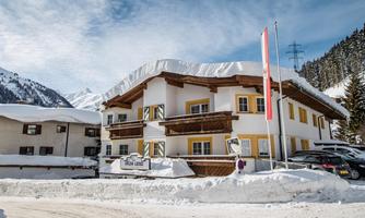 A cozy hotel in the snow with a white roof and colorful windows. Mountains can be seen in the background.