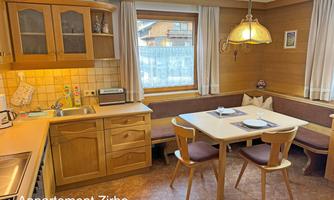 A cozy kitchen with wooden cabinets and a dining table. The window lets in plenty of daylight, and the room is designed to be inviting.