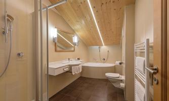 A modern bathroom with a wooden ceiling and elegant furnishings. There is a shower, a sink, and a bathtub, as well as generous light sources.