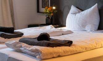 A cozy bedroom with a large bed and clean bedding. On the nightstand, there is a small flower vase and a lamp.