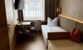 A cozy hotel room with two single beds. There is a table, chairs, and a window with a view outside.