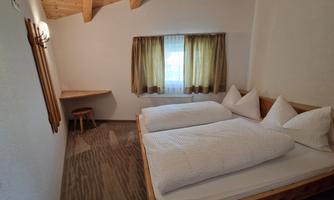 A cozy guest room with two beds and bright wooden decor. The room has a window with curtains and a small table.