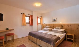 A cozy bedroom with a large bed and wood paneling. The windows are adorned with curtains and the floor is made of wood.