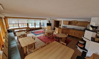 A cozy room with wooden furniture, tables, and benches.  
Large windows let in plenty of light and create an inviting atmosphere.