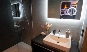 A modern bathroom with an elegant sink and a lit mirror. The shower is adorned with gray tiles and offers a contemporary look.