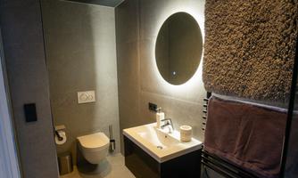 A modern bathroom with a bright, minimalist design. There is a sink, a toilet, and a towel holder with fluffy towels.