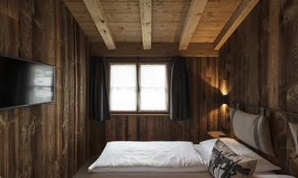 A cozy bedroom with wooden walls and a large window. There is a double bed and a TV on the wall.
