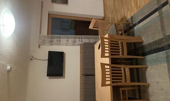 A cozy dining area with a wooden table and four chairs. A gray couch and a television on the wall complete the room.