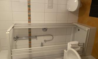 A modern bathroom with a shower cabin, a sink, and a toilet. The walls are brightly tiled and decorated with a colorful stripe.
