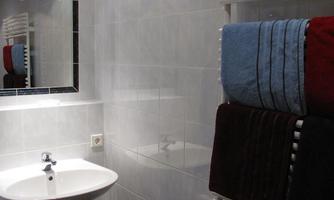 A modern bathroom with white tiles and a sink. Towels in various colors hang on a towel warmer.