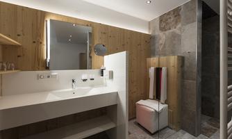 A modern bathroom with wood and stone cladding. It features a sink, a mirror, and a walk-in shower.