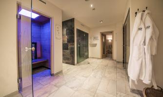 A modern spa with a sauna area and several showers. Soft bathrobes hang on the wall, the walls are bright and welcoming.