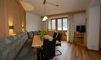 A cozy dining area with a long wooden table and black chairs. Large windows let in plenty of light and offer a view of the surroundings.