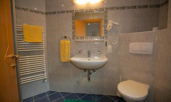 A modern bathroom with blue tiles, a sink, and a shower cabin. Yellow towels and a green rug are also present.