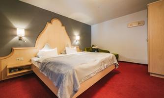 A cozy hotel room with a double bed and a green sofa. The walls are painted in neutral colors, creating a relaxed atmosphere.